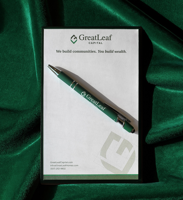 Photos of print collateral showcasing the GreatLeaf Capital branding. Materials include a branded folder, business cards and a notepad, all featuring predominantly rich green colors.