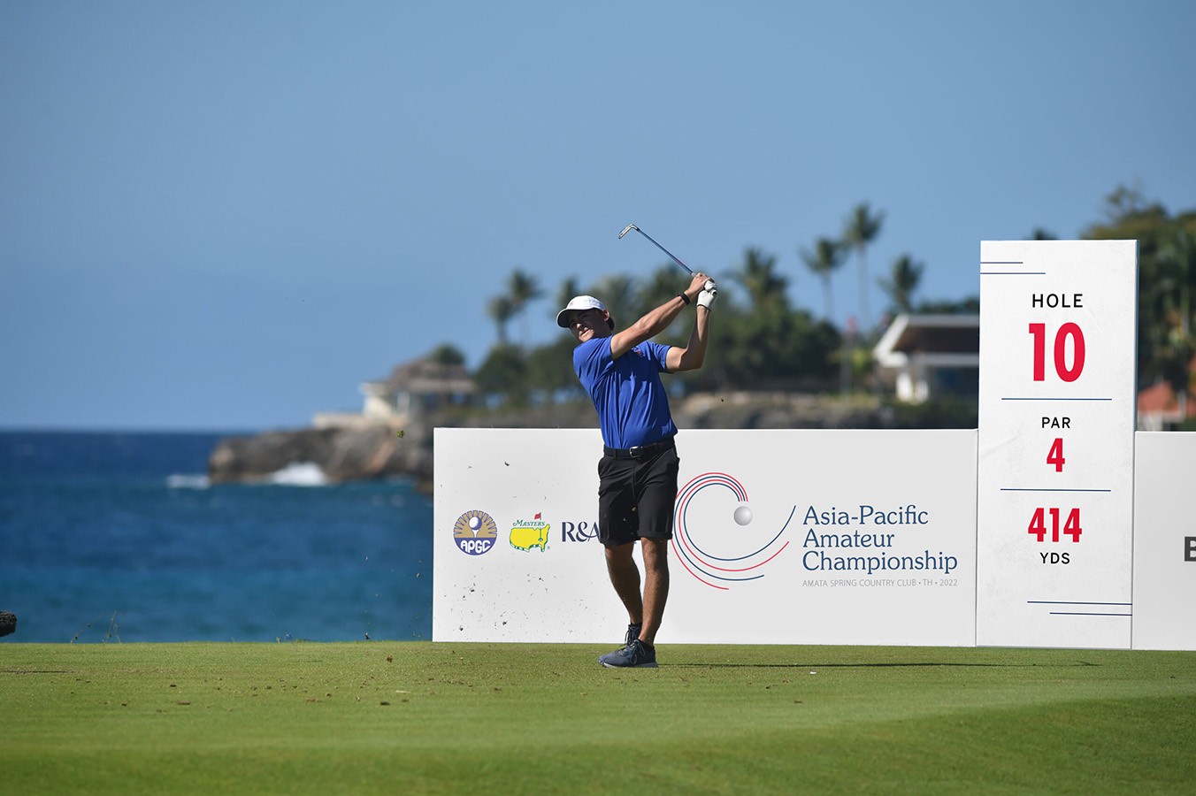 wide outdoor shot of golfer swinging club on a golf course with APAC event graphics behind him.